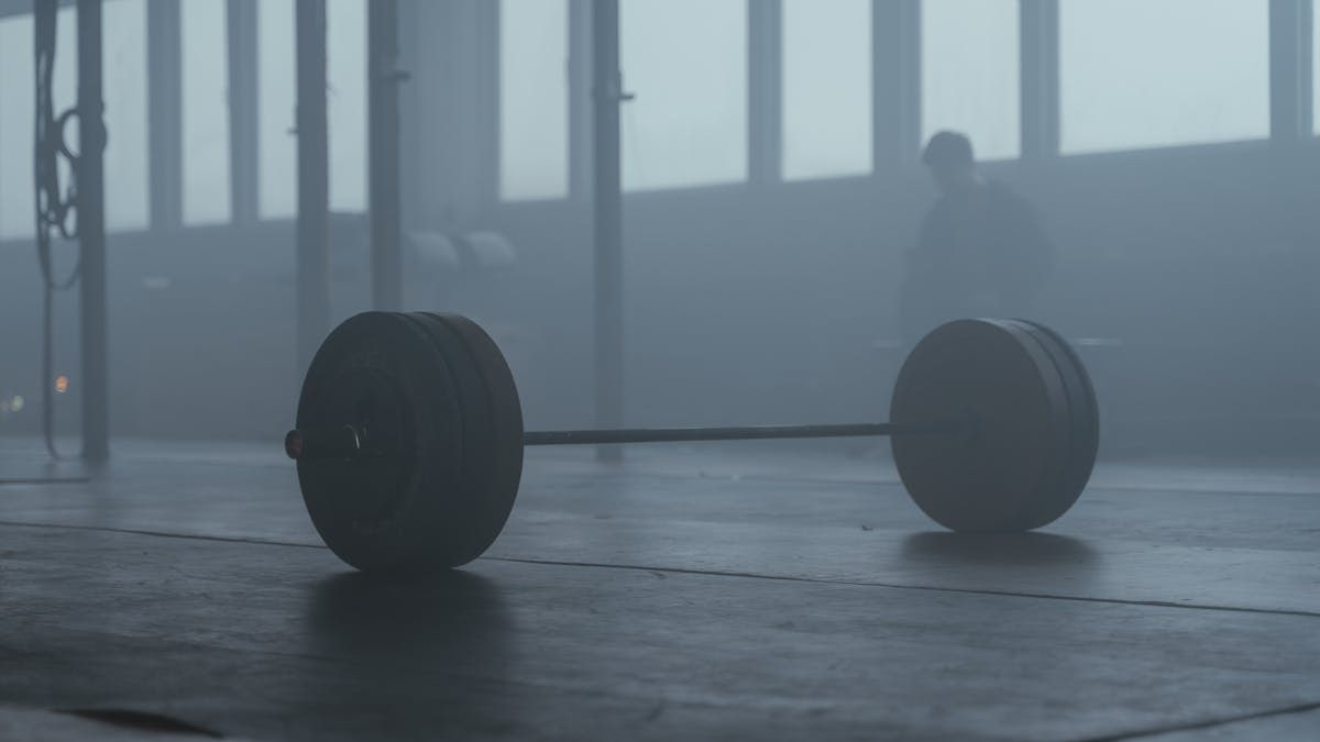 A lone barbell on the gym floor with a misty background creates a mysterious and moody ambiance.